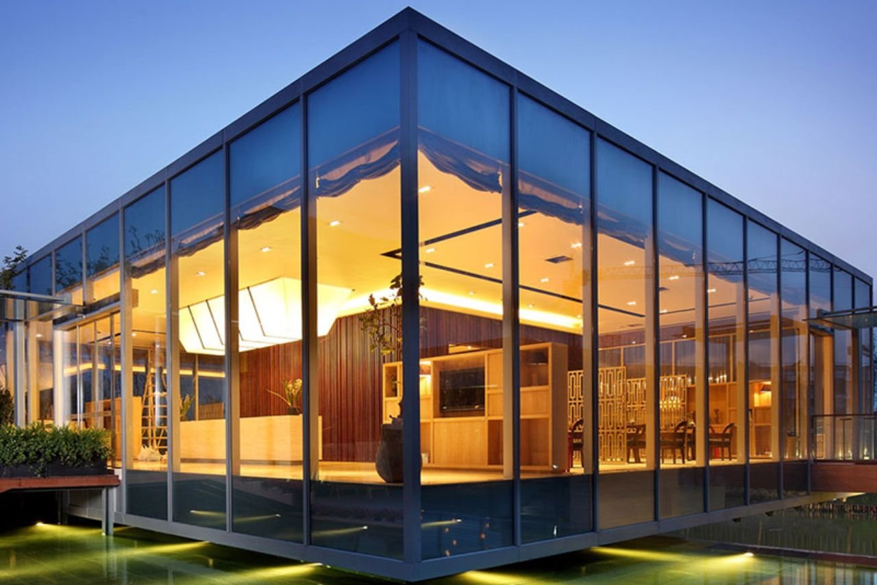 Modern glass building with window and door system illuminated at dusk, showcasing sleek architecture and warm interior lighting